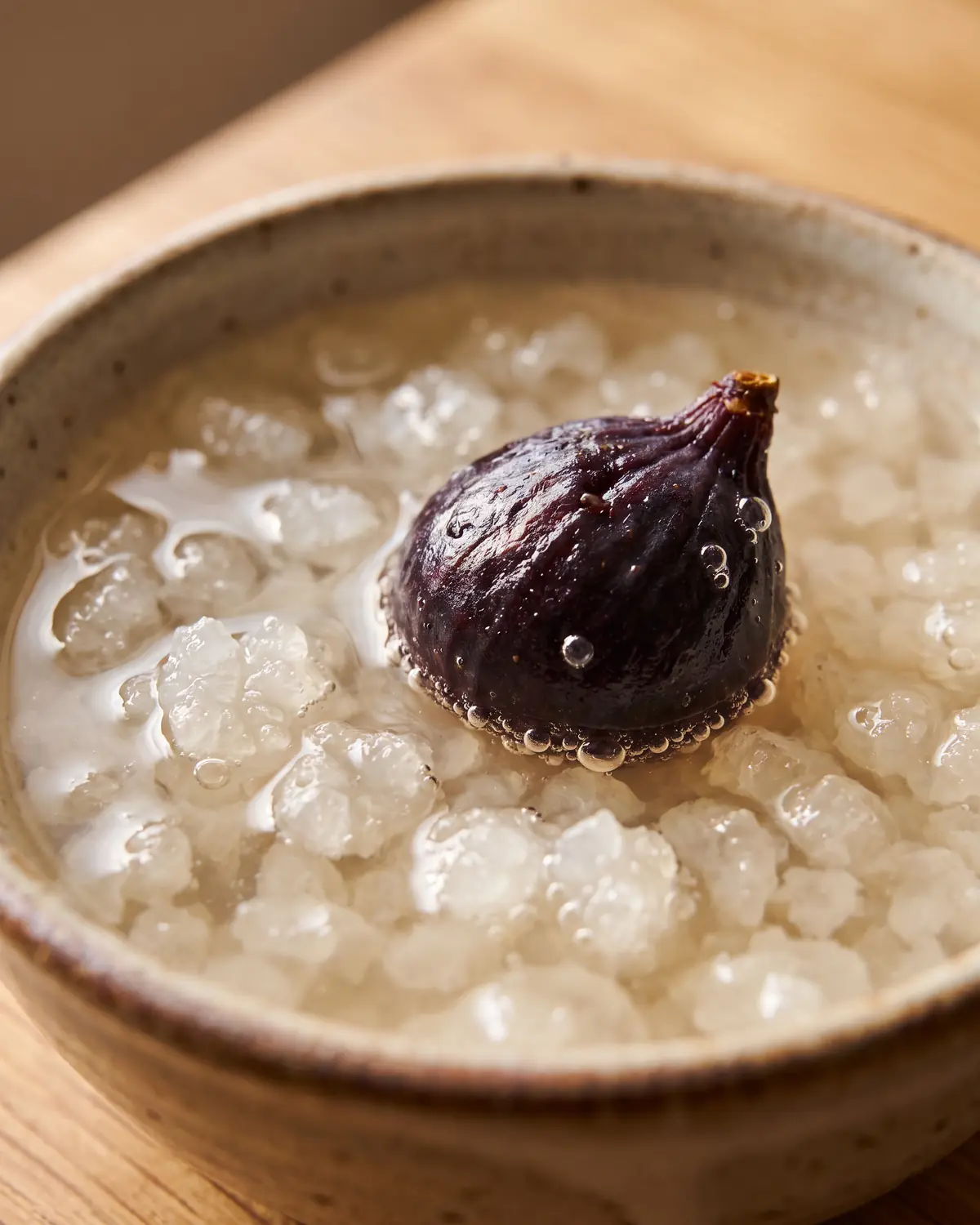 Figue s&egrave;che r&eacute;hydrat&eacute;e flottant au-dessus des grains de k&eacute;fir d&rsquo;eau, avec de fines bulles visibles.