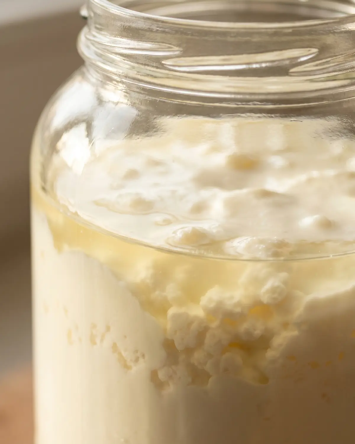 Gros plan d&rsquo;un pot de k&eacute;fir de lait montrant la s&eacute;paration nette entre le s&eacute;rum et la cr&egrave;me.