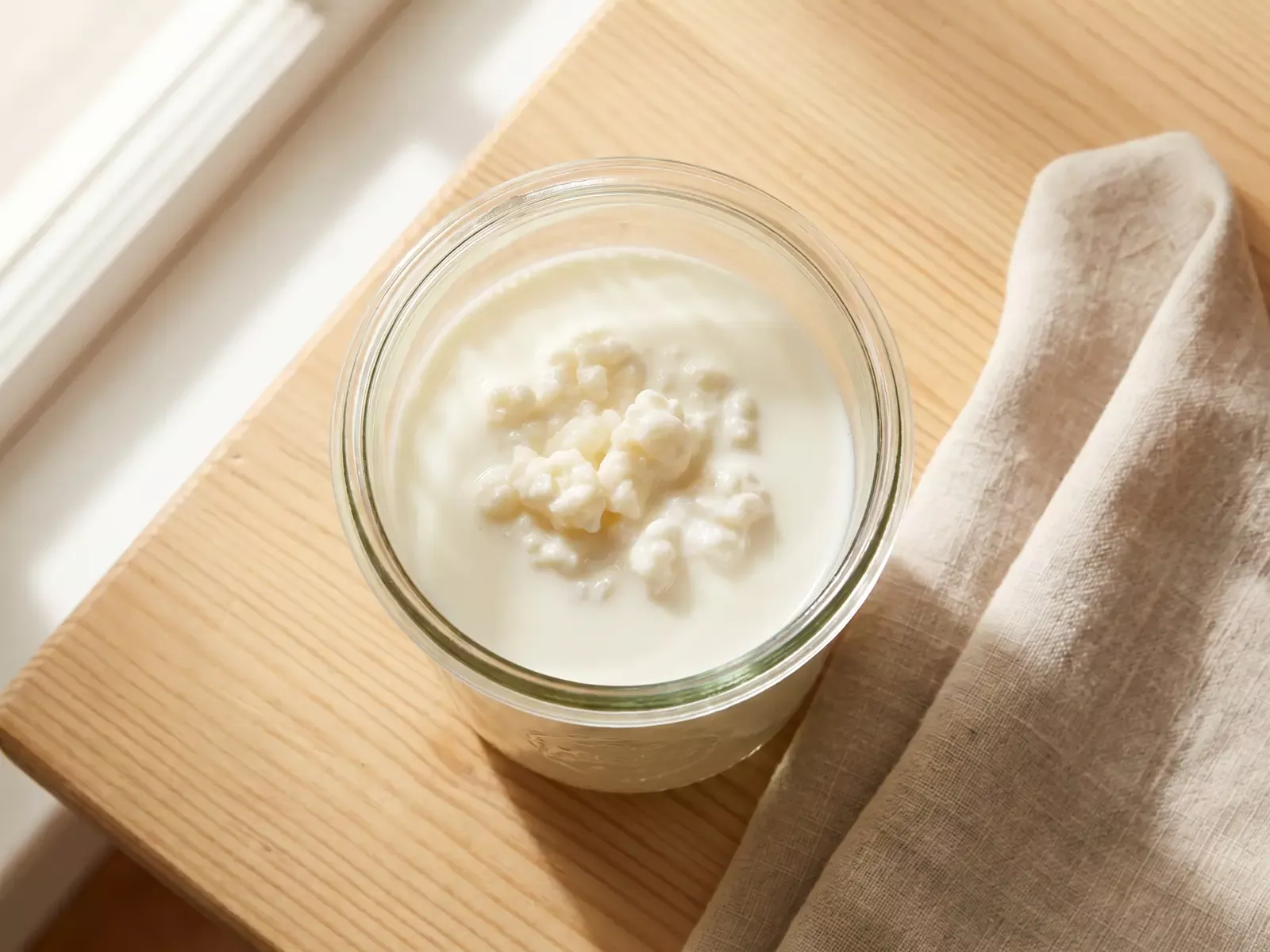 Bocal de k&eacute;fir de lait vu de dessus, en fermentation sur une table en bois avec un linge de lin.