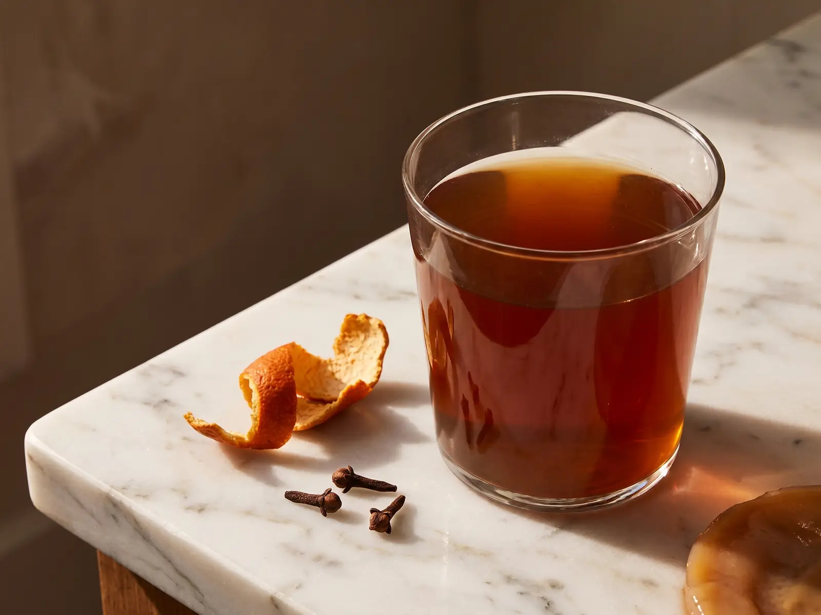 kefir kombucha Verre de kombucha ambré avec clou de girofle et écorce d’orange sur marbre blanc en lumière douce