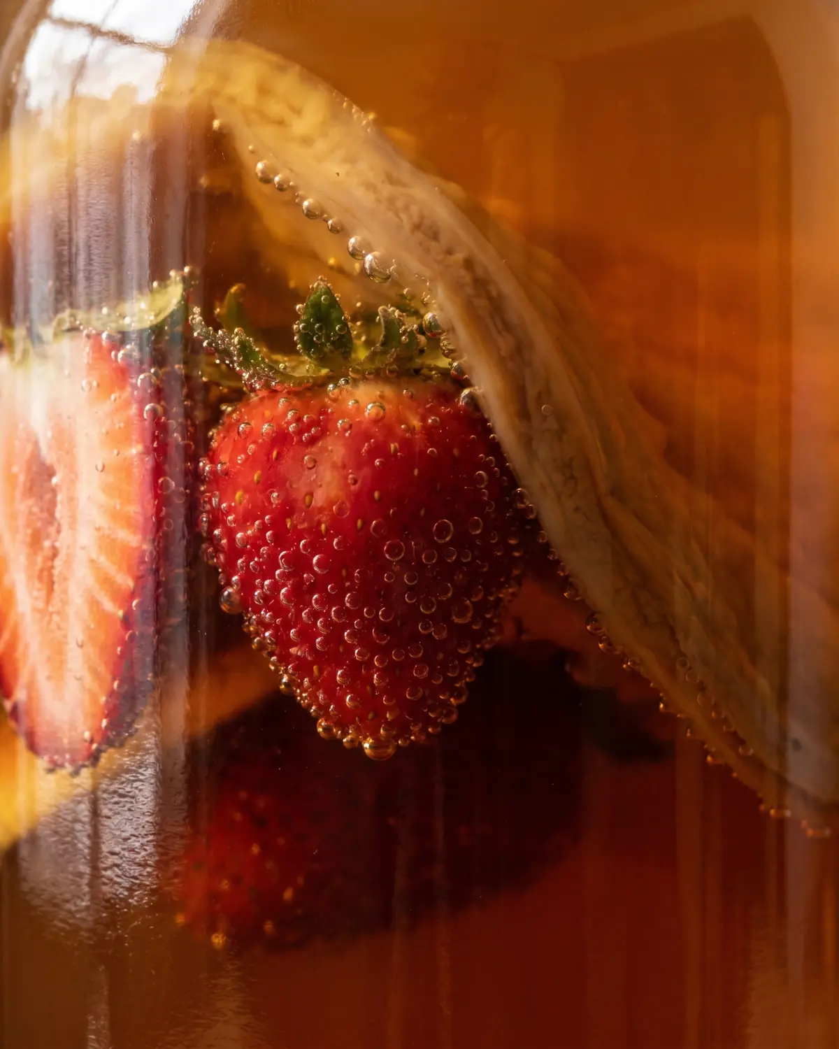 boisson kombucha bienfaits Détail d’une fraise dans une bouteille de kombucha, entourée de fines bulles contre le verre.