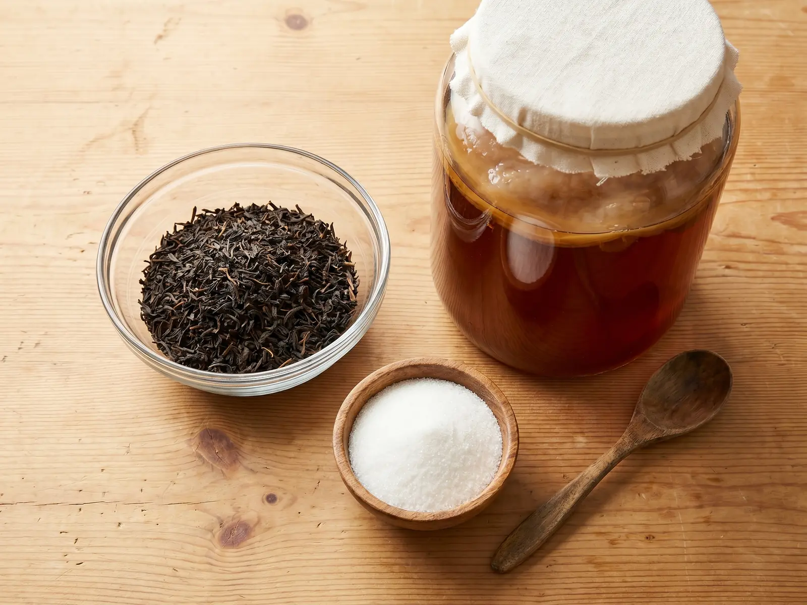 kombucha danger Vue de dessus de feuilles de thé en vrac près d’un bocal de thé sucré prêt à fermenter.
