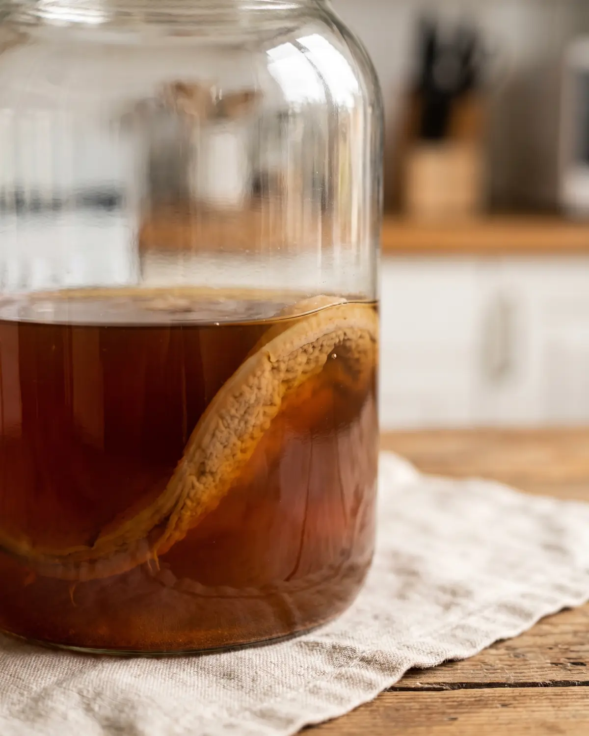 D&eacute;tail ambr&eacute; du kombucha dans un bocal, avec un SCOBY beige affleurant &agrave; la surface.
