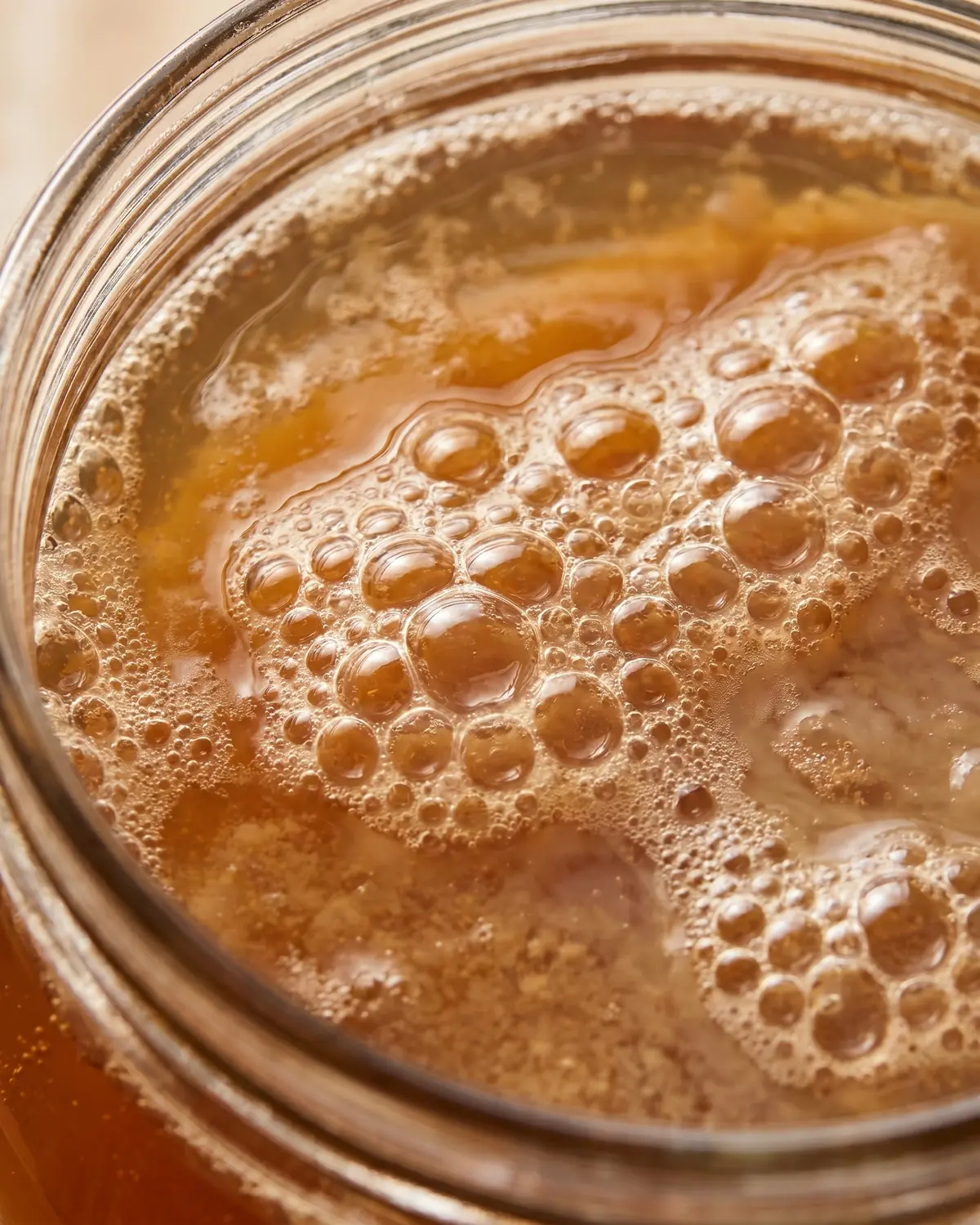 Macro de fines bulles &agrave; la surface d&rsquo;un kombucha ambr&eacute;, avec le bord du verre partiellement visible.