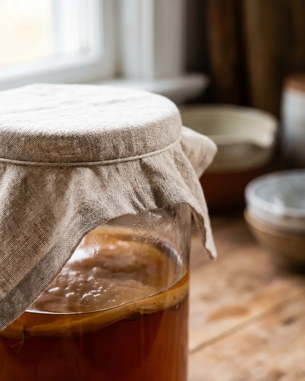 kombucha conservation après ouverture Gros plan sur un tissu tendu couvrant un bocal de kombucha, avec le SCOBY flou sous le thé ambré.