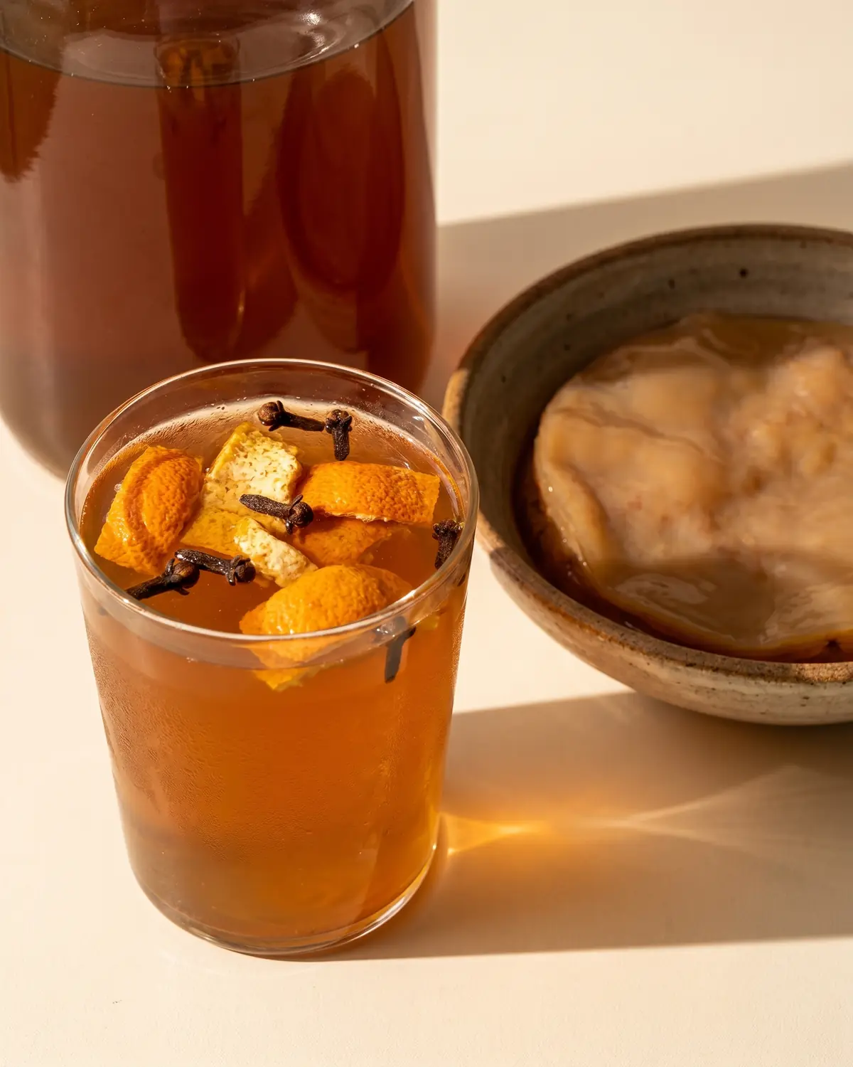 kombucha bienfaits perte de poids Verre de kombucha ambré avec peau d’orange séchée et clou de girofle dans une lumière douce de fin de journée.